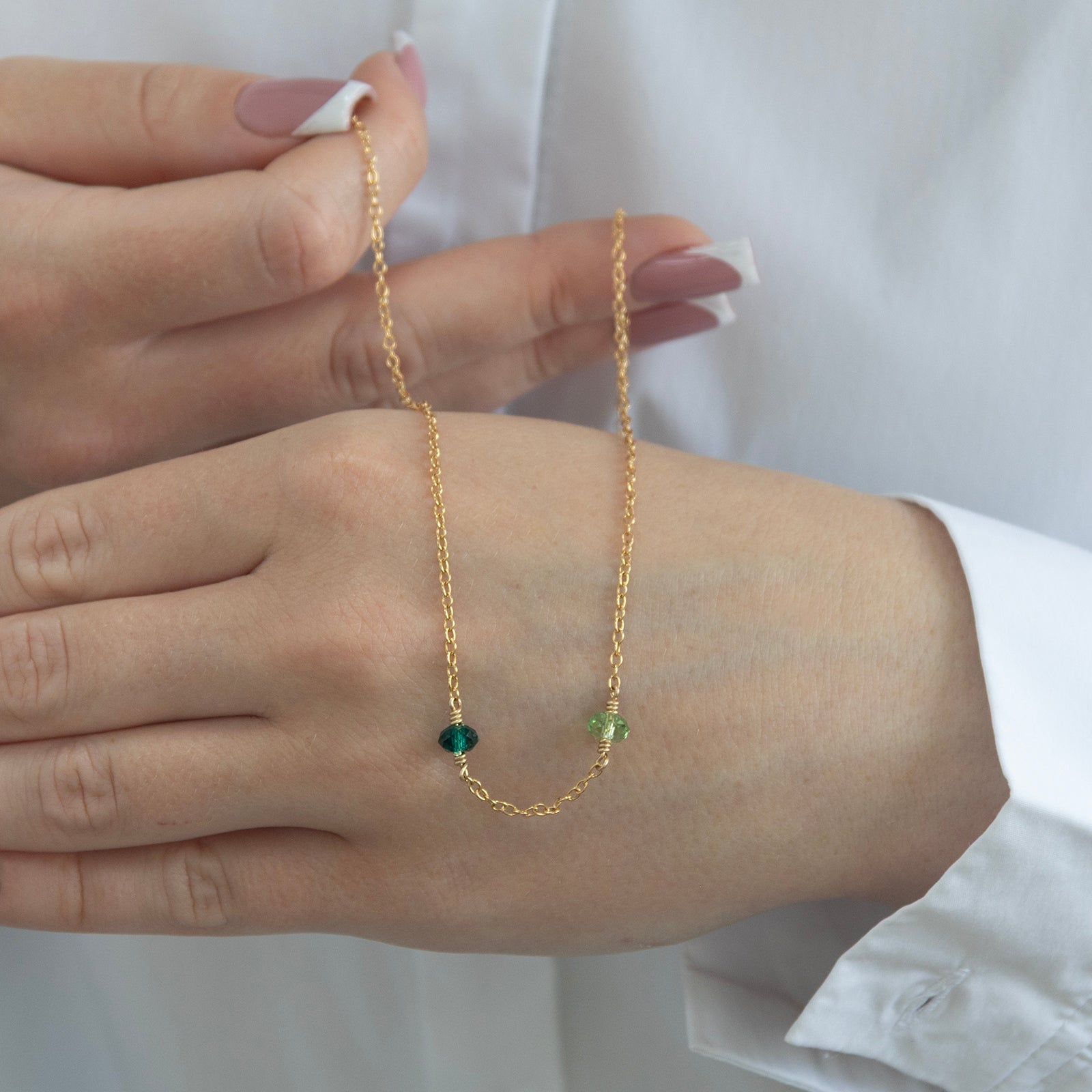 family birthtstone necklace with two birthstones in gold in a models hand 